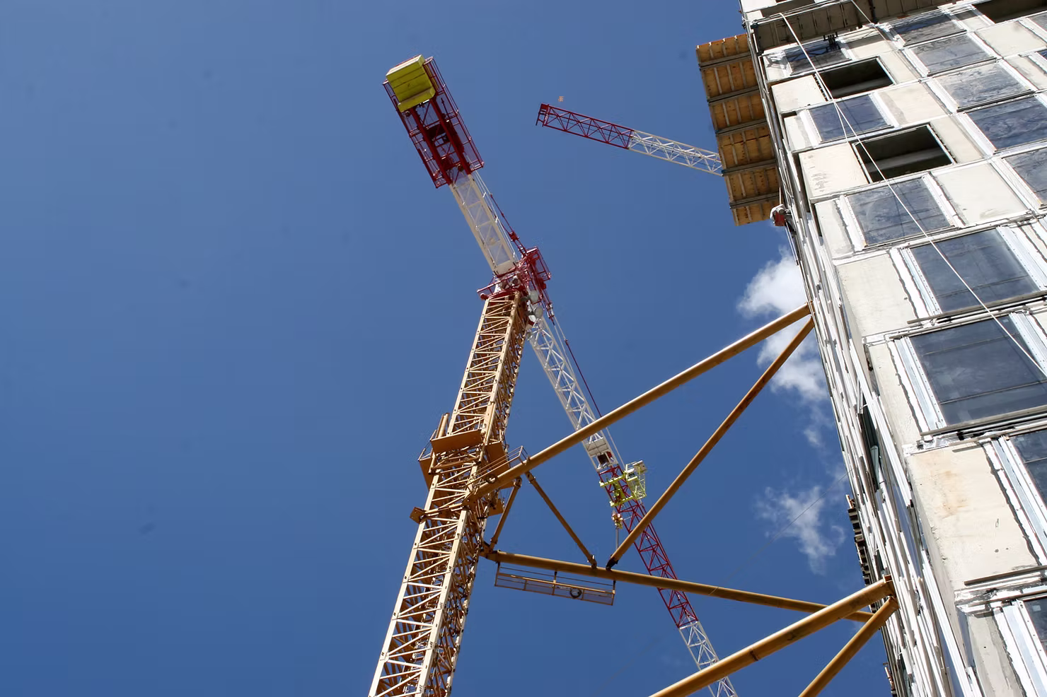 Low-angle view of a tower crane braced against a high-rise building under construction beneath a clear blue sky
