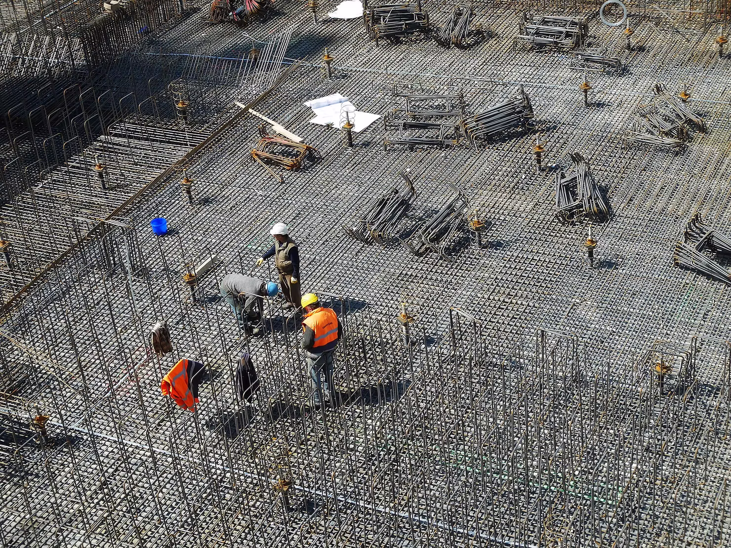 Aerial view of construction workers in hard hats tying a vast grid of steel rebar for a concrete foundation slab