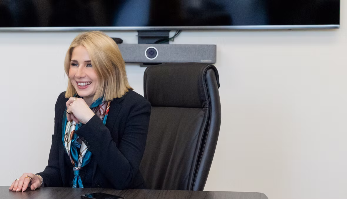 Arvaya CEO Ashlee Jack smiling at a conference table in a black blazer and teal silk scarf