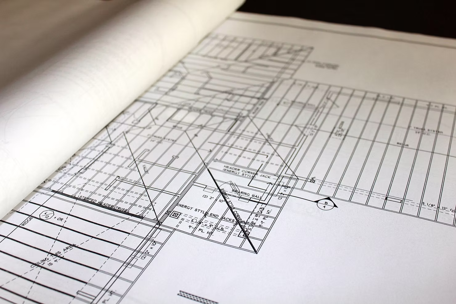 Close-up of a partially unrolled architectural framing plan showing roof trusses, headers, and bearing wall notes