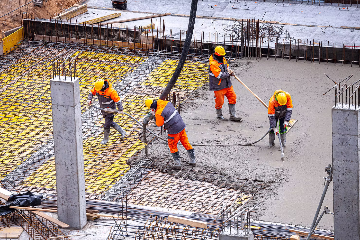 Construction crew in hard hats and high-visibility gear pouring and leveling a concrete slab over rebar on a building site